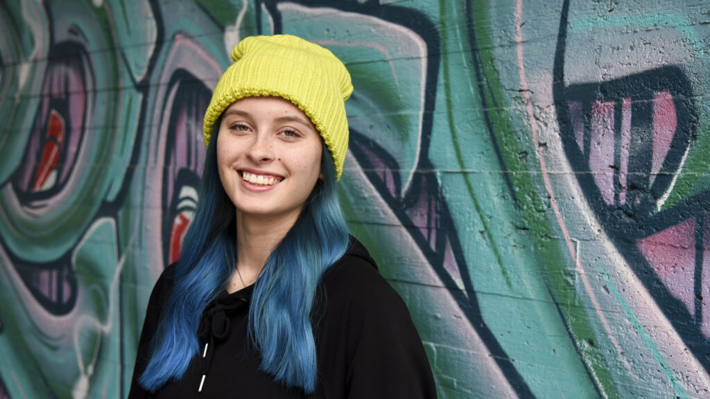 Young girl stands in front of a colourful wall.